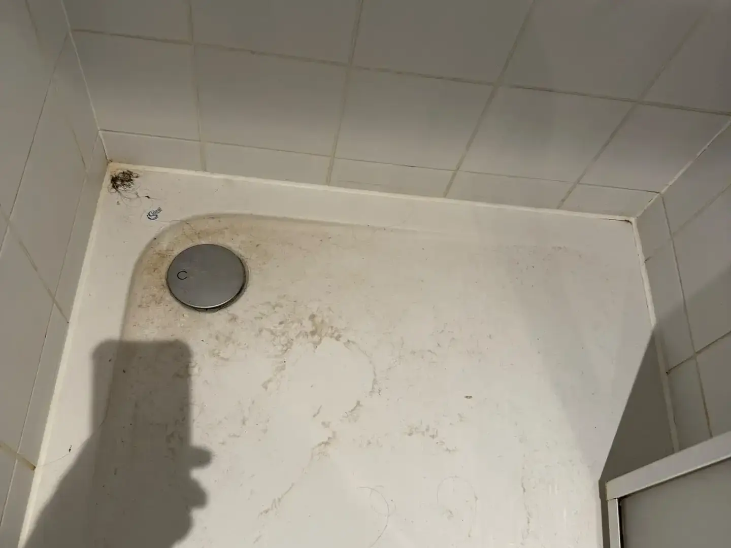 Receveur de douche avant intervention : dépôts et cheveux autour de la bonde.