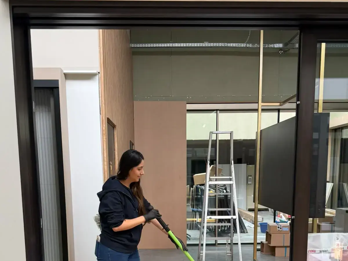 Une opératrice passe la serpillière sur un sol en bois dans un espace en fin de chantier, échelle et cartons encore en place.